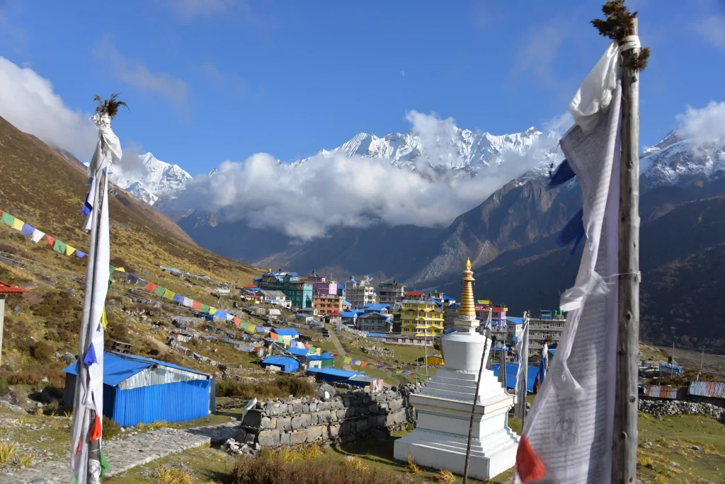 A Buddhist stupa and Kyanjin Gompa surrounded by snow-capped Himalayan mountains during the Langtang Valley Trek in Nepal.